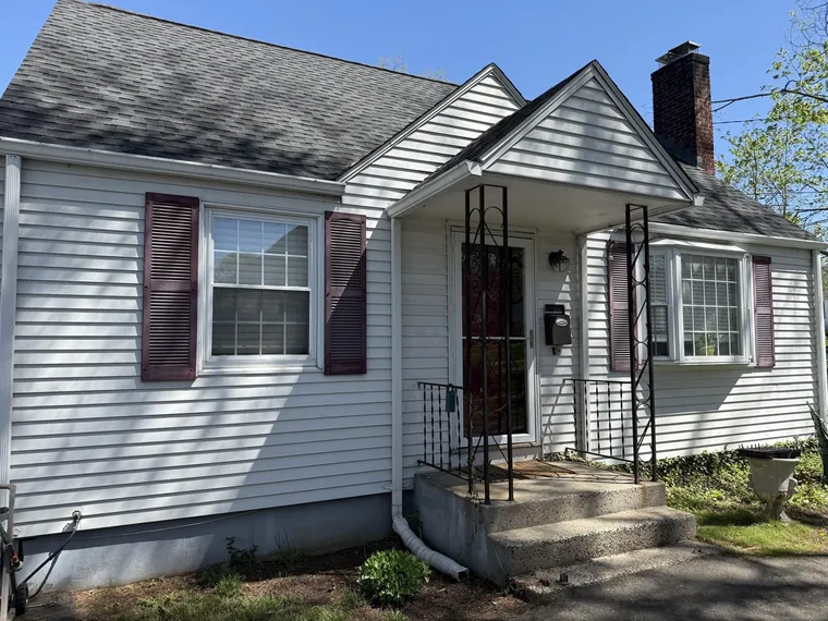White vinyl-sided Cape Cod home with maroon shutters, a brick chimney and a covered front step at 1029 N Worthy Street, Windsor, Connecticut